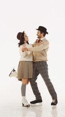 Stylish couple, man and woman wearing retro-styled clothes and headwear, dancing on ice rink, having fun and enjoying cozy date. Concept of winter, vacation, holiday, leisure activity