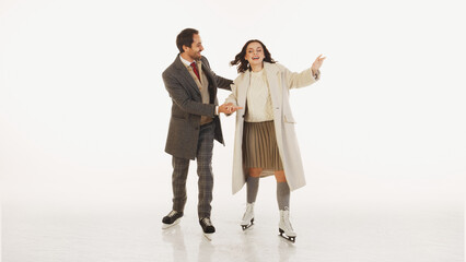 Stylish man and woman enjoying time together, ice skating isolated on white background. Couple wearing stylish, warm clothes. Concept of winter, vacation, holiday, leisure activity