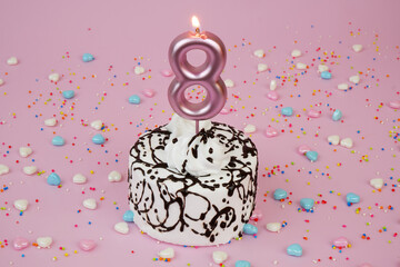 Birthday cake with burning candle number 8 and many sprinkles on pink background.