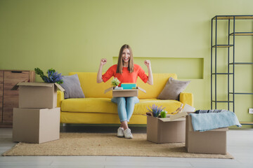 Full body photo of nice young girl sit sofa unpacking winning wear orange clothes enjoy modern bright cozy spring interior flat indoors