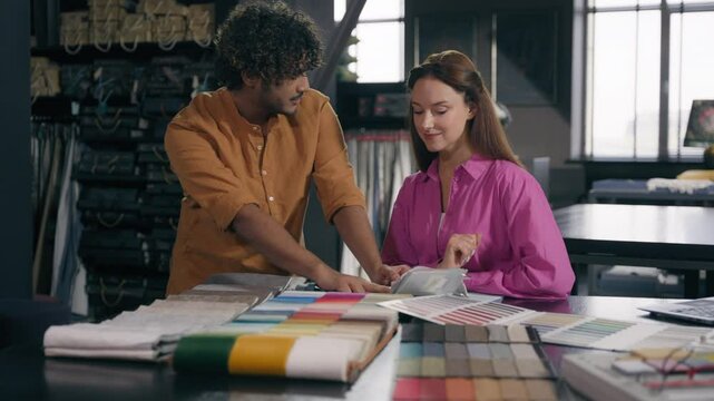 Multiracial couple buyers Arabian man Caucasian woman girl guy coworkers male fashion designer female tailor choosing cloth garment in atelier buying fabric in shop choose textile samples collection