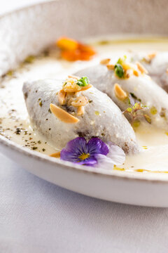 Kibbeh in creamy white sauce garnished with nuts and fresh herbs.