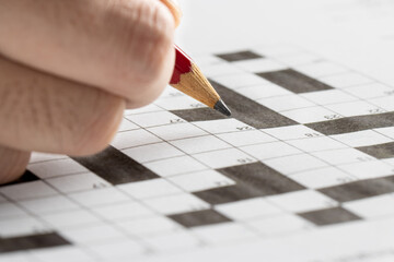 hand holding red pencil, try to write an answer on crossword puzzle. Black and white crossword puzzle. On black background. 