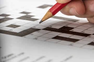 hand holding red pencil, try to write an answer on crossword puzzle. Black and white crossword puzzle. On black background. 