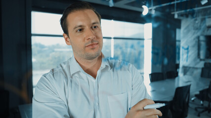 Smart businessman thinking about start up project in front of glass board. Smiling male project...