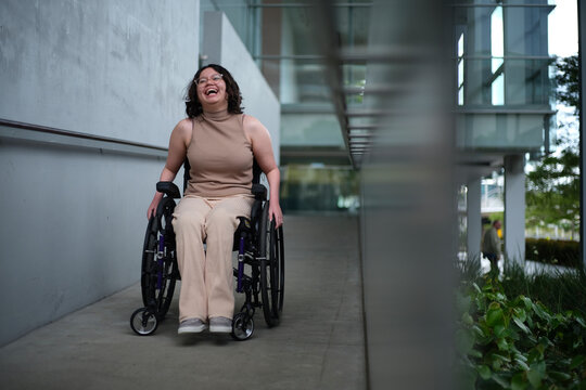 Smiling woman with a disability sitting in a wheelchair doing down the accessibility ramps