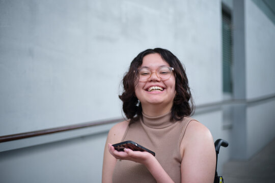 Smiling woman with a disability sitting in a wheelchair indoors holding a mobile phone