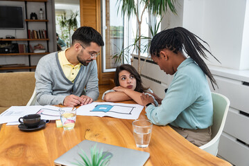 Fototapeta premium Diverse group of smiling young business people working together on a laptop during a meeting in modern small office. Businessman and businesswoman work on new innovative project of cheap housing.