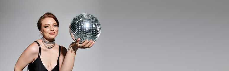 Naklejka premium A stylish young woman in an elegant outfit confidently holds a shimmering disco ball.