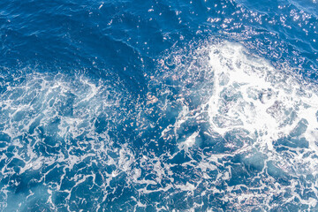 Sunlight glistens on deep blue ocean waves, with seafoam adding a dynamic texture and sparkle.