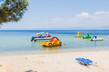 Serene beach scene featuring colorful pedal boats floating on calm, crystal-clear waters.