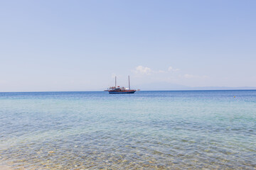 Large sailboat filled with passengers glides smoothly over the crystal-clear blue waters on a bright sunny day