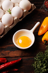 Bright YelloVibrant orange yolk in a white pan-shaped sauce dish, surrounded by eggs, pepper, and fresh greens on a rustic wooden backgroundw Egg Yolk in Pan-Shaped Sauce Dish. High quality photo