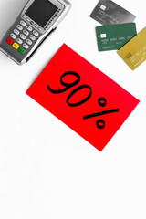Sales concept with discount sing. Online shopping - white table with POS payment terminal and credit cards, top view