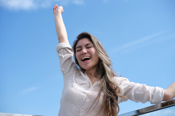 Close-up photo of a woman happily leaning against the glass fence on the rooftop with one hand up