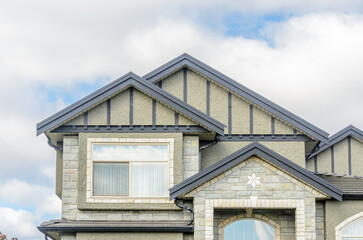 Top of grey stucco luxury house with shingle roof, red and yellow trees and nice windows in Summer in Vancouver, Canada, North America. Day time on June 2024.