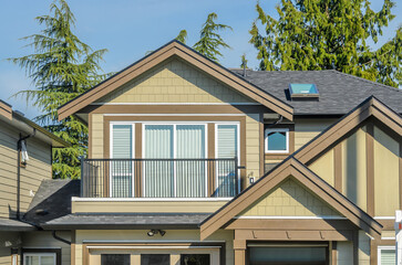Top of grey stucco luxury house with shingle roof, red and yellow trees and nice windows in Summer in Vancouver, Canada, North America. Day time on June 2024.