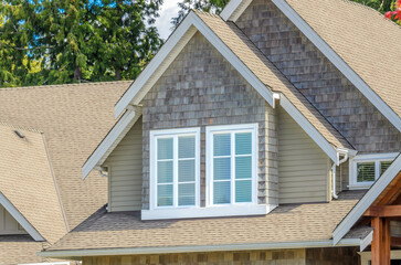 Top of grey stucco luxury house with shingle roof, red and yellow trees and nice windows in Summer in Vancouver, Canada, North America. Day time on June 2024.