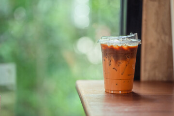 Glass of iced milk tea with coffee on woodden. table in coffee shop.