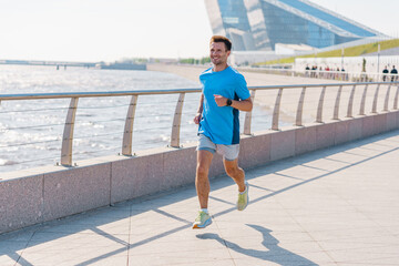 A Man Jogging Along a Waterfront Promenade on a Sunny Day in the City With Modern Architecture in...