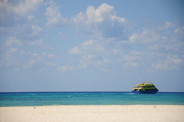 Obraz premium Ferry cruises through turquoise waters of Playa del Carmen beneath clouds