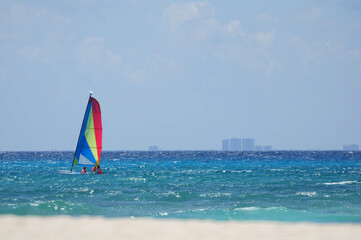 Colorful sailboat gliding across the turquoise ocean under a clear blue sky.