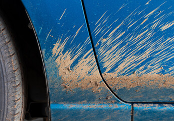 close-up shot of a muddy blue sedan captures the rugged exterior, showcasing dirt splattered across the wheels and body, emphasizing its recent journey through challenging off-road terrain.