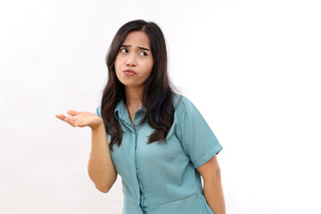 Fototapeta premium Indignant displeased Asian woman concentrated away has sad expression raises hand with clueless look wears casual shirt earrings poses against white background copy space for text or promotion