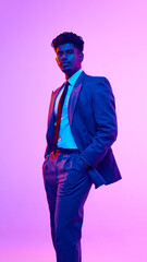 Full-length portrait of confident, young, Indian man in formal wear, standing with hands in pockets, against purple studio background in neon light. Concept of emotions, lifestyle, business, education