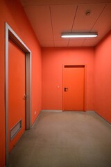 empty narrow room with red walls on gray floor and two closed doors