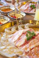 A woman uses tongs to pick up fresh shrimps to grill in Thai style, called Moo Kratha in Thai. The set includes pork, chicken, shrimp, squid, and bacon.