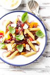 Penne pasta with yellow and red pepper, hard cheese and fresh basil. Bright background. Close up.	