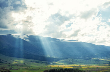 Sun rays breaking through clouds, illuminating a valley and mountains