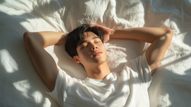 An Asian man with short-cropped hair, lying comfortably on a bed with his hands behind his head, in a room filled with clean, minimal decor and soft shadows