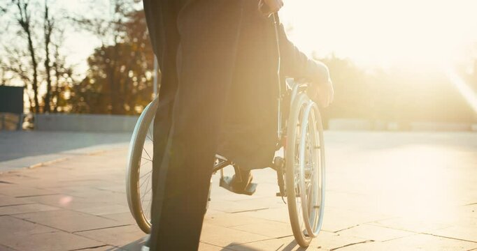 Hispanic man taking care of old disabled friend in wheelchair. Friends spending time together in autumn park. Healthcare, disability, mobility, friendship. Close up 4k shot