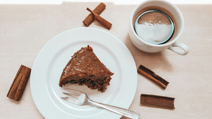 Slice of a cinnamon cake on a white plate next to a cup of coffee and sunlight reflection