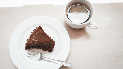 Slice of a cinnamon cake on a white plate next to a cup of coffee and sunlight reflection