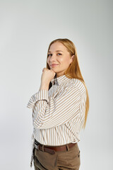 A fashionable woman with long hair stands gracefully, wearing a striped top and pants, exuding confidence.