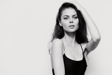 Fototapeta premium Young woman with long hair in a black top, striking a confident pose against a plain white background. Emphasis on beauty and self-expression.