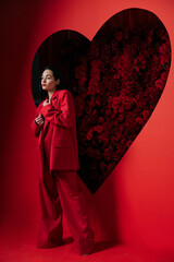Beautiful girl posing on red background decorated by heart shape with red roses.