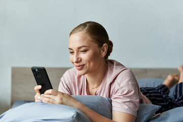 A young woman lounges comfortably on her bed, engaging with her smartphone and smiling.