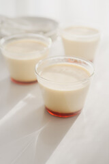 homemade Japanese caramel custard pudding in a glass cup on white  table in morning sunlight.