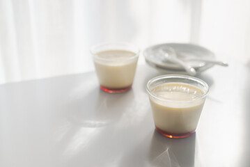 homemade Japanese caramel custard pudding in a glass cup on white  table in morning sunlight.