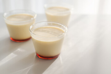 homemade Japanese caramel custard pudding in a glass cup on white  table in morning sunlight.