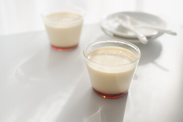 homemade Japanese caramel custard pudding in a glass cup on white  table in morning sunlight.