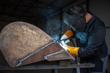 Metal worker welding metal part wearing protective gear