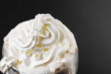 Whipped cream is squeezed out of a can onto a rotating cup of coffee on a black background....