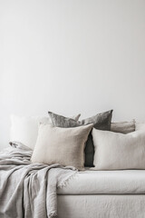 Soft, neutral-toned blankets complement an elegant sofa adorned with linen and natural fabric cushions. Set against a plain white wall, the scene emphasizes the beautiful textures.