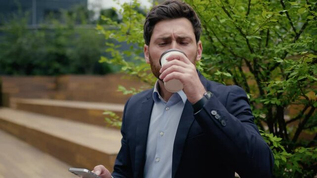 Caucasian man business employer office manager sit outside drinking coffee male guy businessman client entrepreneur using mobile phone in city outdoors bad drink disgust upset with tasteless beverage