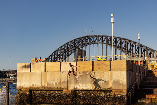 Kid jumping from ledge into water with Sydney Harbour Bridge in background